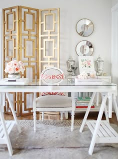 a white desk topped with a chair next to a wall covered in mirrors and pictures