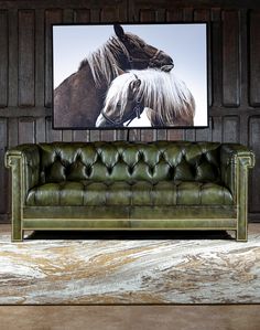 a green leather couch sitting in front of a framed horse photo on the wall above it