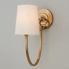 a wall light with a white shade on it's side and a gold finish