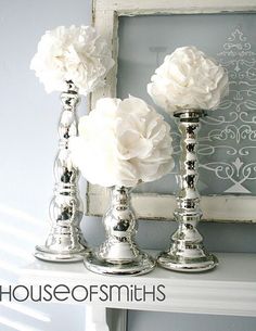 three silver candlesticks with white flowers in them sitting on a shelf next to a mirror