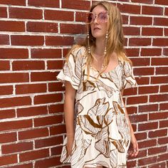 Featuring a brown tropical print set on a white cotton fabrication, this top is sure to keep you looking fab and feeling comfy all season long. The tiered design coupled with the loose short sleeves creates a flowy and beautifully feminine silhouette. With an open back and adjustable neck ties, this versatile tunic transitions from Saturday night to Sunday morning with ease!  Whether you wear this dress around town or to brunch with the girls, you're guaranteed to look and feel like a bohemian queen! Quality: 100% Cotton Care Instructions: Hand wash cold or dry clean. Air dry flat on a hanger or tumble dry on low heat. Brown Printed Tops For Vacation, Printed Brown Tops For Vacation, Summer Tiered Tops For Vacation, Casual Tiered Tops For The Beach, Casual Tiered Tops With Floral Print, Casual Tiered Floral Print Top, Casual Tiered Tops For Vacation, Brown Floral Print Tops For Beach, Summer Brown Tops With Floral Print