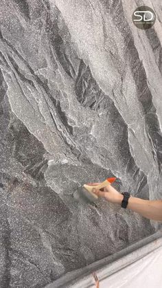 a person holding something in their hand near a large stone wall that looks like granite