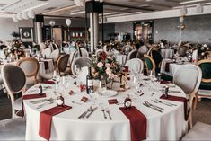 a dining room with tables and chairs covered in white tablecloths, red napkins and place settings