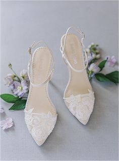 a pair of white shoes sitting on top of a table next to flowers and greenery