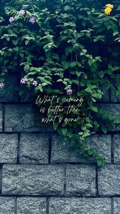 a brick wall with flowers growing on it and a sign that says, what's coming is better than what's gone