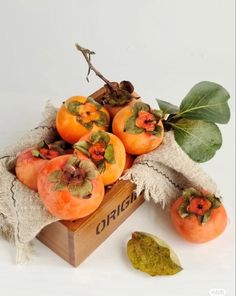 some oranges are in a wooden box on a white surface with green leaves around them