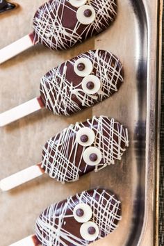 four chocolate covered candy sticks with googly eyes on them, sitting in a metal tray