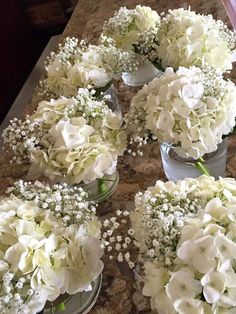 white flowers are arranged in glass vases on a counter top, ready to be used as centerpieces