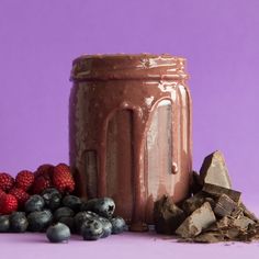 a jar filled with chocolate next to some berries and other foods on a purple surface