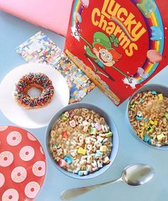 cereal in bowls next to a box of lucky charms and a plate with a donut