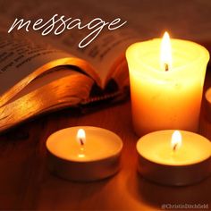 three lit candles sitting on top of a table next to an open book with the words message