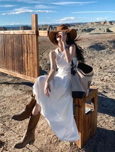 a woman in a white dress and cowboy hat sitting on a bench with her hands to her face