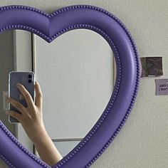 a heart shaped mirror hanging on the wall above a woman's hand holding a cell phone