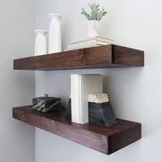 two wooden shelves with books, vases and rocks on them in a white room