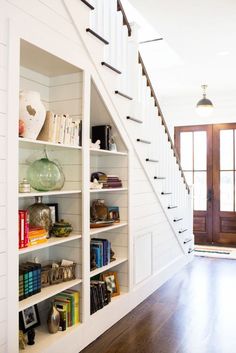 an open book shelf with books on it in the middle of a room next to a staircase