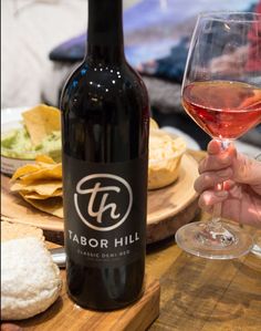 a person holding a glass of wine in front of a bottle and cheese platter