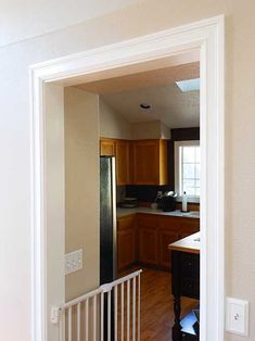 an open door leading to a kitchen with wooden cabinets and white trim on the walls