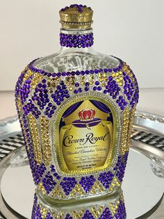 a glass bottle covered in purple and gold beads with a crown on it's top