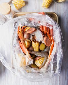 a plastic bag filled with crab legs, corn on the cob and carrots