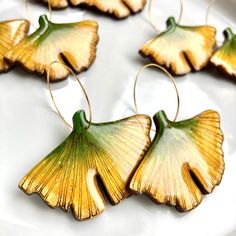 four yellow and green leaf shaped earrings on a white plate