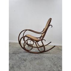 a wooden rocking chair sitting on top of a cement floor next to a white wall