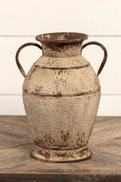 an old brown vase sitting on top of a wooden table next to a white wall