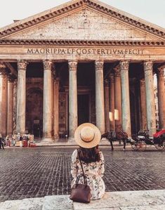 a woman with a hat sitting in front of a building that has columns and pillars