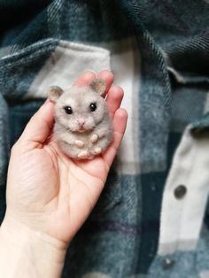 a person holding a tiny hamster in their hand on a plaid cloth covered surface