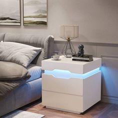 a white night stand sitting on top of a wooden floor next to a gray couch