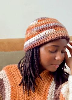 a woman with dreadlocks is wearing an orange and white crochet hat