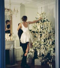 a man and woman are decorating a christmas tree in the living room with white bows