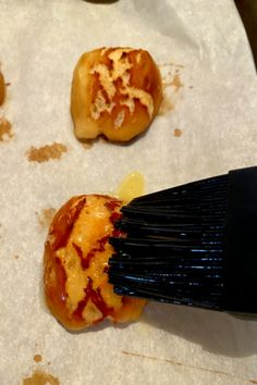 someone is using a brush to spread sauce on pastries that are sitting on wax paper