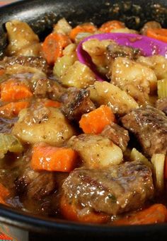 a bowl filled with meat and vegetables on top of a checkered table cloth next to a spoon