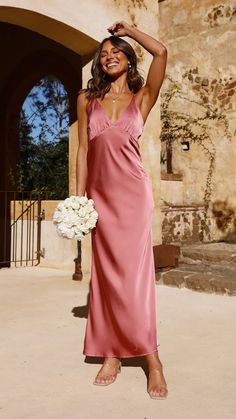 a woman in a long pink dress holding a bouquet of flowers and posing for the camera