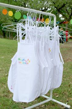 several white shirts hanging on a rack in the grass with balloons and streamers behind them