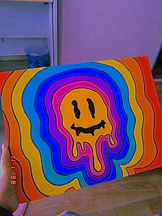 a person holding up a colorful painting with a smiley face on it's side