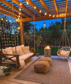 an outdoor living area with swing chairs, rugs and lights on the patio at night