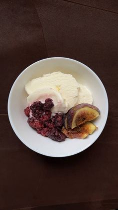 a white bowl filled with fruit and ice cream on top of a wooden table,