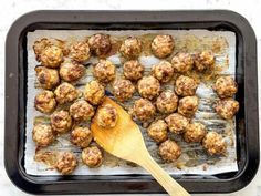 a wooden spoon sitting on top of a baking pan filled with meatball patties