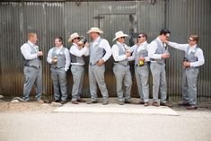 a group of men standing next to each other in front of a metal wall wearing ties and hats