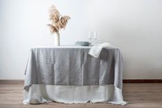 a table topped with a white cloth covered table next to a vase filled with dry grass