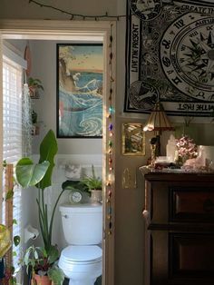 a white toilet sitting in a bathroom next to a wooden dresser and window covered with plants