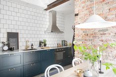 a kitchen with brick walls and blue cabinets, white tile backsplash, gold accents