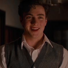 a young man is smiling and wearing a vest