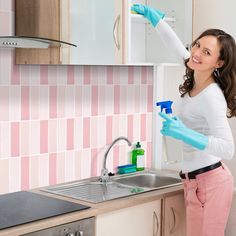 a woman in pink pants and blue gloves cleaning a kitchen sink with a spray bottle