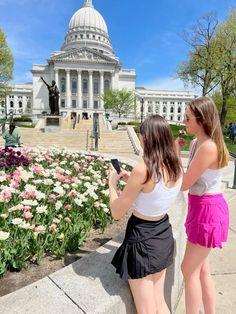 two girls are looking at their cell phones in front of the state capitol building