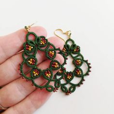 a pair of green and red earrings on a hand with gold earwires in the shape of circles