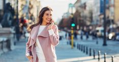 a woman is walking down the street talking on her cell phone and smiling at the camera