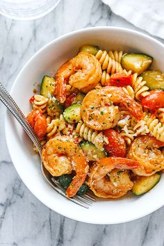 pasta with shrimp, zucchini and tomatoes in a white bowl on a marble table