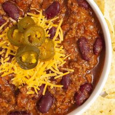 a white bowl filled with chili and cheese next to tortilla chips on a table